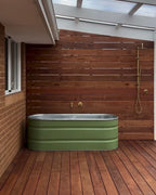 Green stock tank bathtub in an outdoor room with wooden floor and wall.