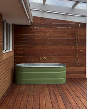 Green stock tank bathtub in an outdoor room with wooden floor and wall.