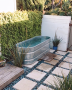 Outdoor setting with a metal bathtub on a stone patio surrounded by plants and greenery.