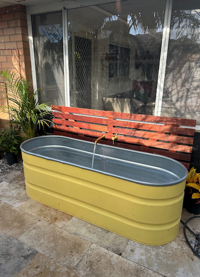 Yellow metal stock tank tub with a red wooden bench in the background