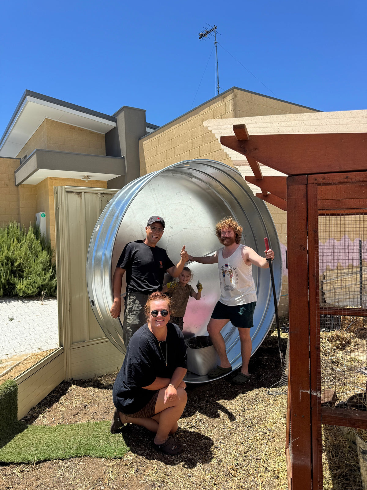 People posing with a large steel stock tank pool in front of a house.