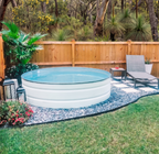 White stock tank pool in a backyard with greenery and a wooden fence.