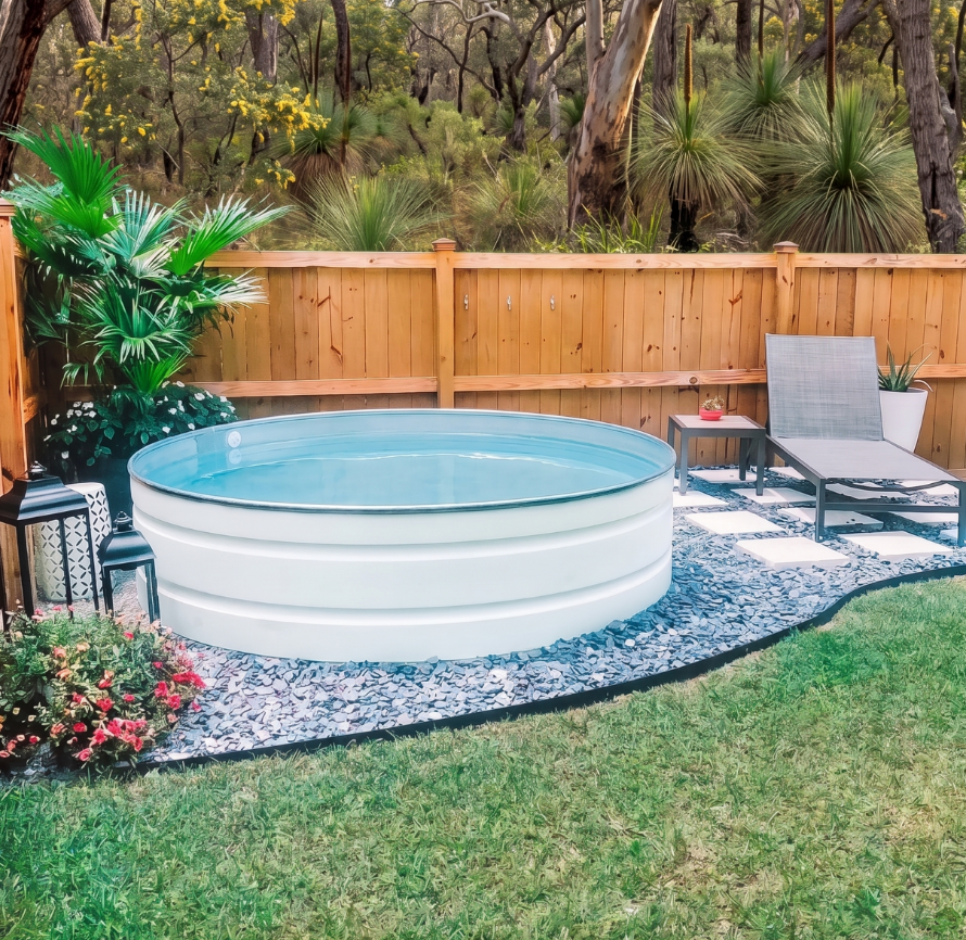 White stock tank pool in a backyard with greenery and a wooden fence.