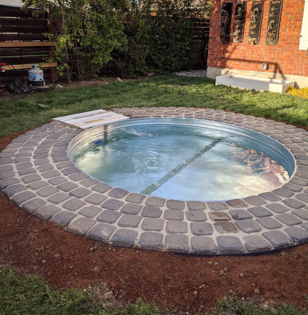 Small stock tank pool with stone patio in a backyard setting